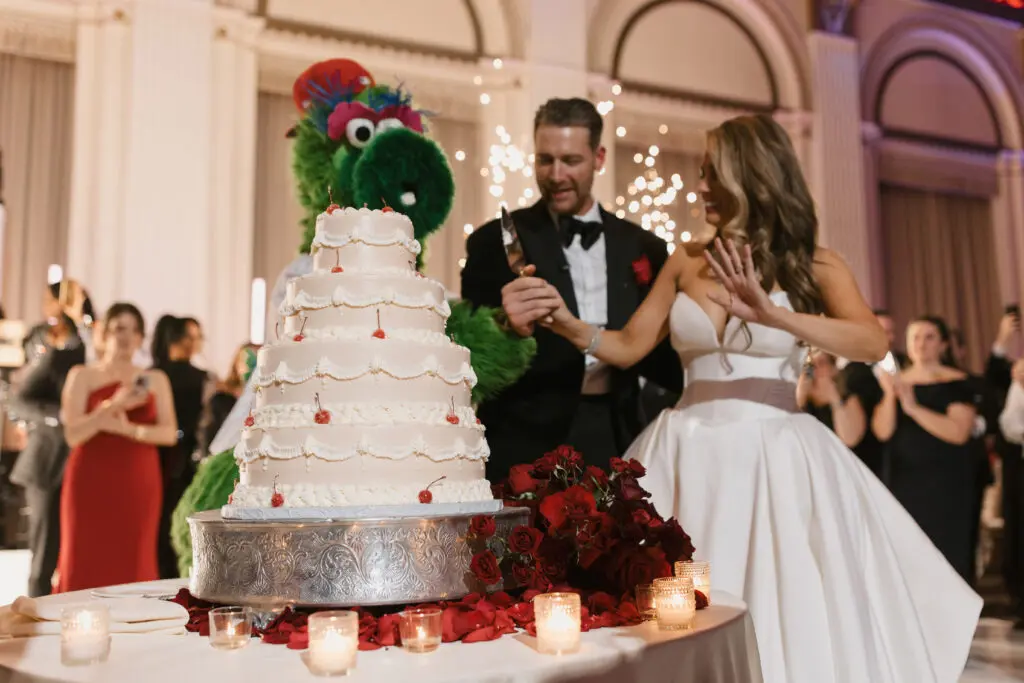 Jessica Boyington and Phillie Phanatic Cutting Cake by Mario Oliveto Photogaphy Bride and Groom cutting wedding cake with Phillie Phanatic