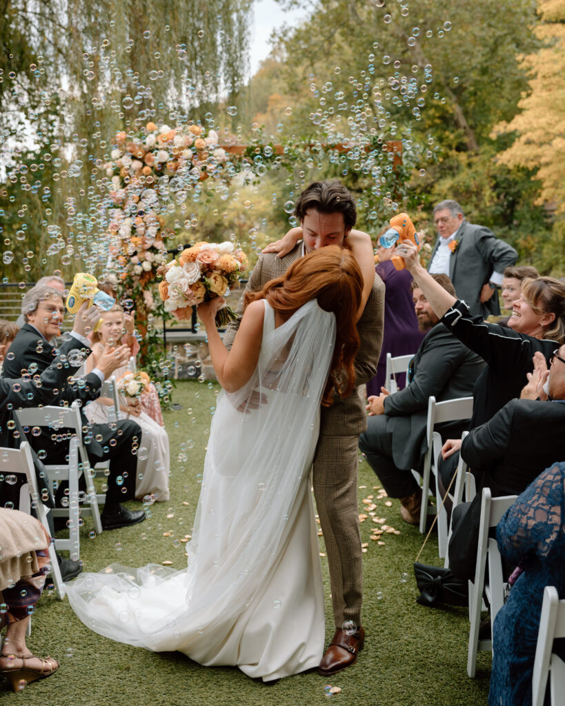 Bride and groom kissing in the aisle with bubbles floating in the air
