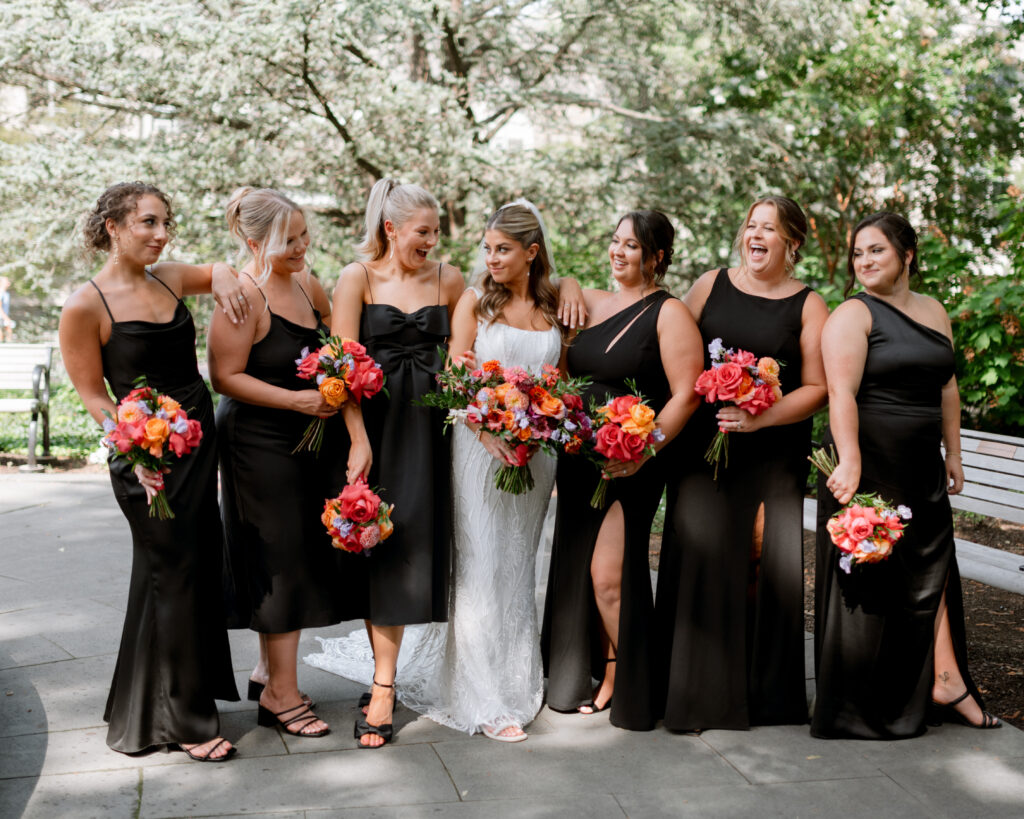 Bridesmaids match in black dresses posing with bride and high impact florals