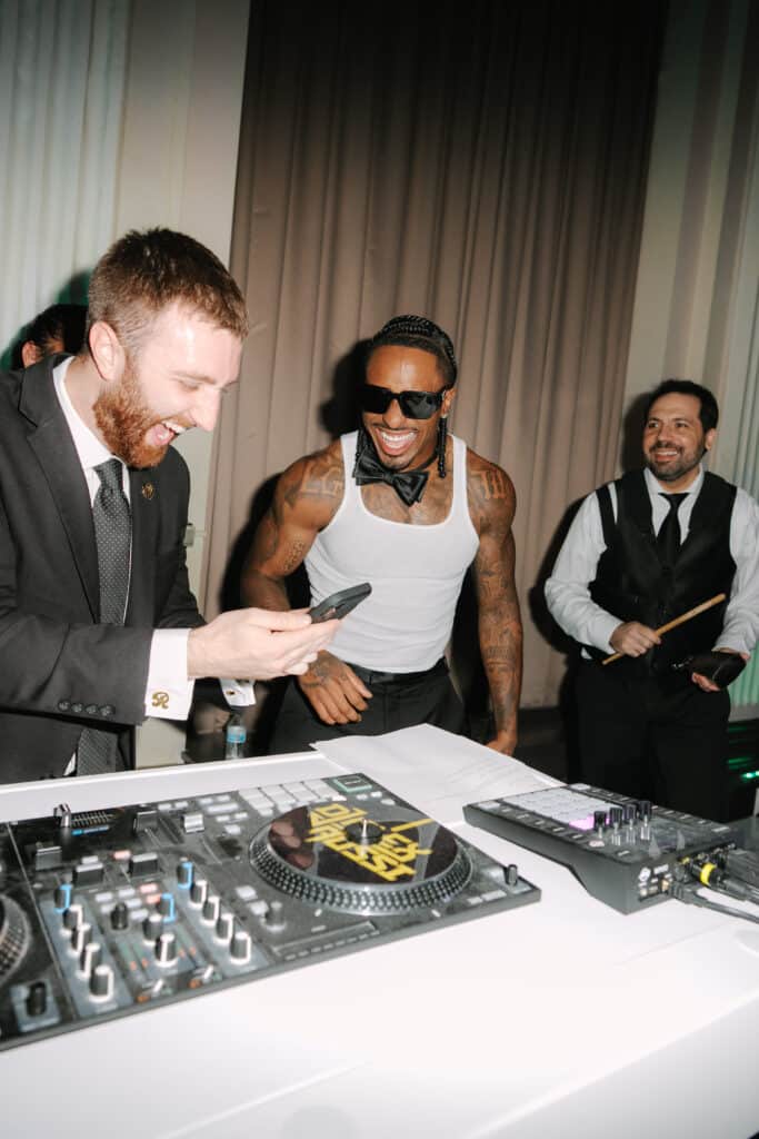 DJ Alex Rossi and KJ Hamler behind DJ booth laughing at wedding